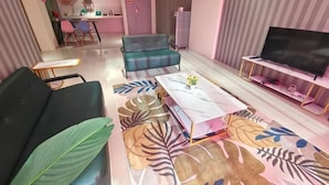 A living room with a sofa, a coffee table with a floral pattern, a television, and a kitchen in the background. - Pavilionvillie M1T570 by Irainbow (Kinta)