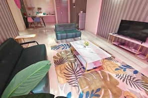 A living room with a sofa, a coffee table with a floral pattern, a television, and a kitchen in the background.