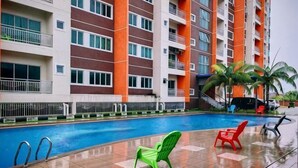 A swimming pool with lounge chairs, a fence, and a multi-story building with balconies. - Pavilionvillie M1T570 by Irainbow (Kinta)
