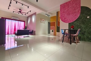 Habitación de hotel moderna con una cama grande, un escritorio y una silla. Se ve una ventana con cortinas, un ventilador de techo y una pared con diseño geométrico.