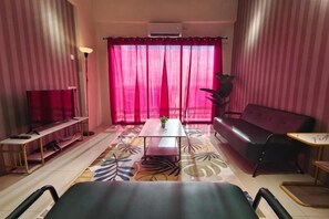 A living room with a sofa, a coffee table, a TV, and a large window with curtains.