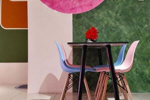 A table with a vase of red flowers, surrounded by colorful chairs, against a green textured wall. - Pavilionvillie M1T570 by Irainbow (Kinta)