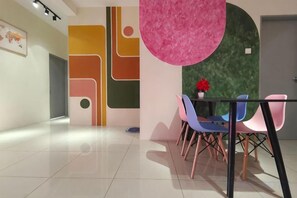 Un espace repas moderne avec une table en verre, des chaises colorées et un mur décoratif orné de motifs géométriques.