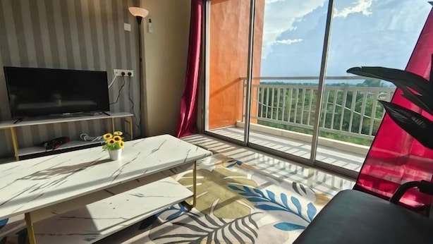 A room with a TV, a table with a vase, a chair, and a balcony with a view. - Pavilionvillie M1T570 by Irainbow (Kinta)