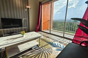 Una habitación con televisión, una mesa con un florero, una silla y un balcón con vistas.