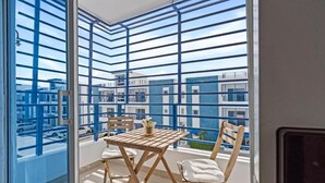 Un balcón con vistas a edificios, una mesa con sillas y una planta en maceta.