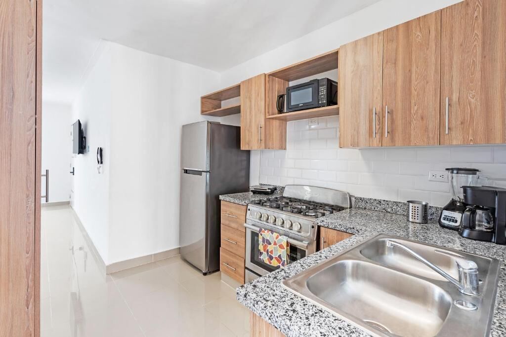 A modern kitchen with wooden cabinets, a stainless steel sink, a microwave, a stove, and a refrigerator.