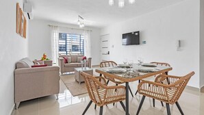 Una sala de estar moderna con un sofá, una mesa de comedor con sillas y un televisor montado en la pared.