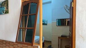 Een kamer met een groot raam, een ventilator en een klein tafeltje.