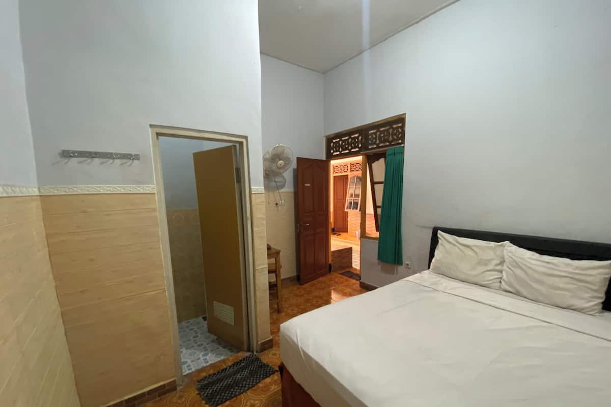 Een slaapkamer met een bed, een houten deur, een ventilator en uitzicht op een balkon.