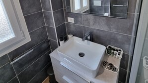 A modern bathroom with dark tiles, a white sink, a mirror, and a window.