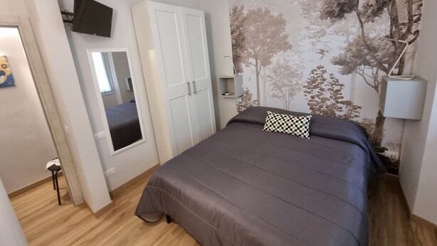 A bedroom with a bed, wardrobe, mirror, and a wall with a tree mural.
