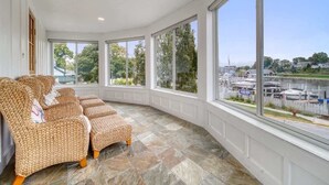 A sunlit room with large windows overlooking a marina, featuring wicker furniture and stone flooring. - Harbor Views, Hot Tub, Walk to Beach, Dog Friendly (South Haven)
