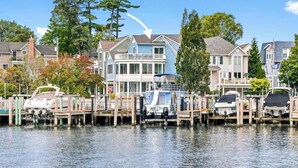 A waterfront property with docked boats, a house with a balcony, and a clear sky. - Harbor Views, Hot Tub, Walk to Beach, Dog Friendly (South Haven)