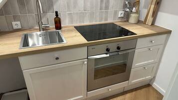 Une cuisine équipée d’un évier en acier inoxydable, d’une plaque de cuisson à induction noire et d’un four Bosch.