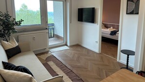 A room with a sofa, a television, a bed, and a view through a sliding door. - Schönblick B7 House · Modern with a Balcony Next to the Ski Lift (Schöfweg)