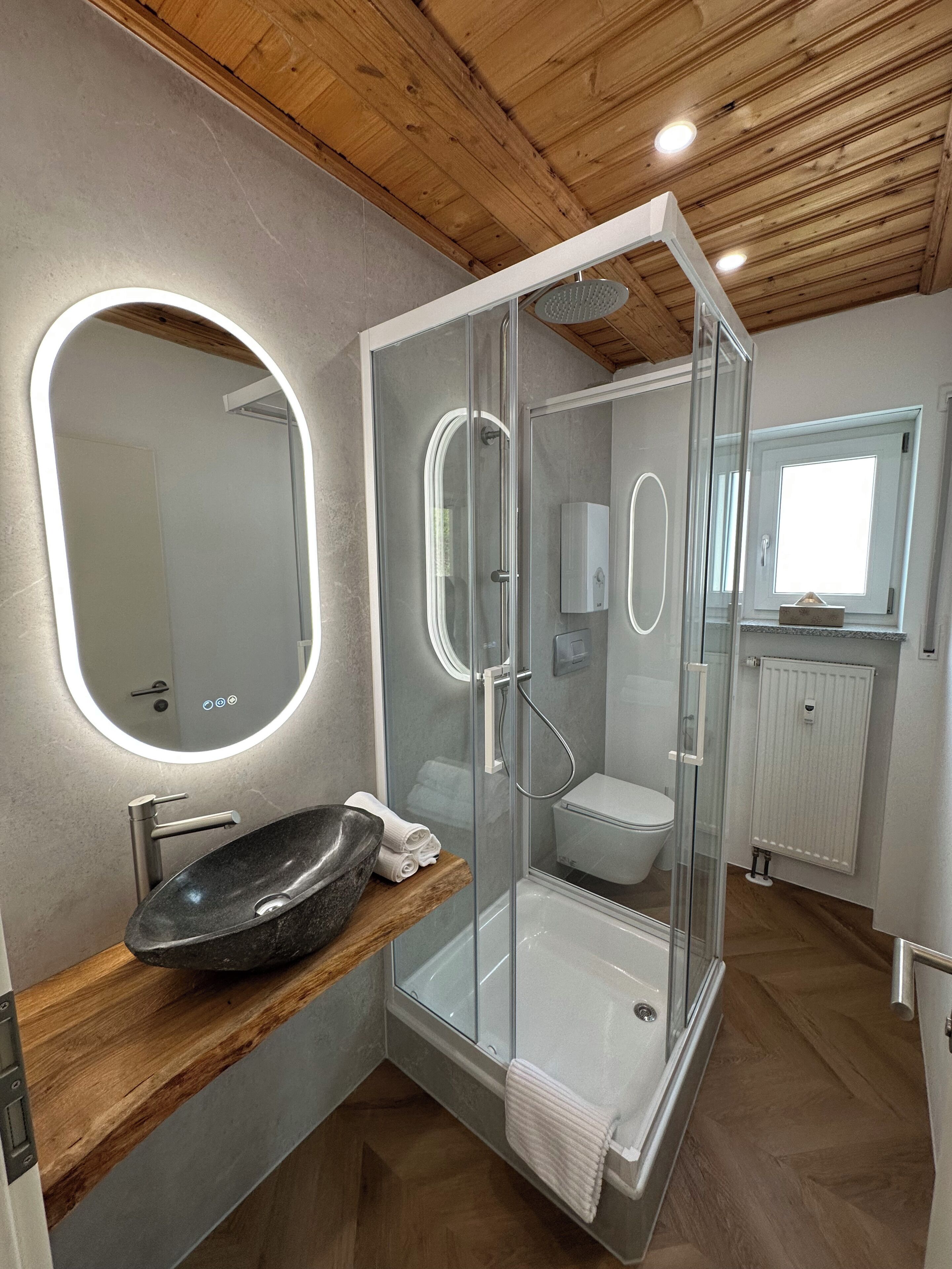Een moderne badkamer met een douche in een glazen cabine, een ronde spiegel en een wastafel.