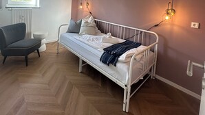 A bedroom with a bed, a chair, a window, and wall-mounted lighting. - Schönblick B7 House · Modern with a Balcony Next to the Ski Lift (Schöfweg)