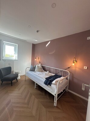 Ein Schlafzimmer mit einem Bett, einem Sessel, einem Fenster und Wandleuchten.