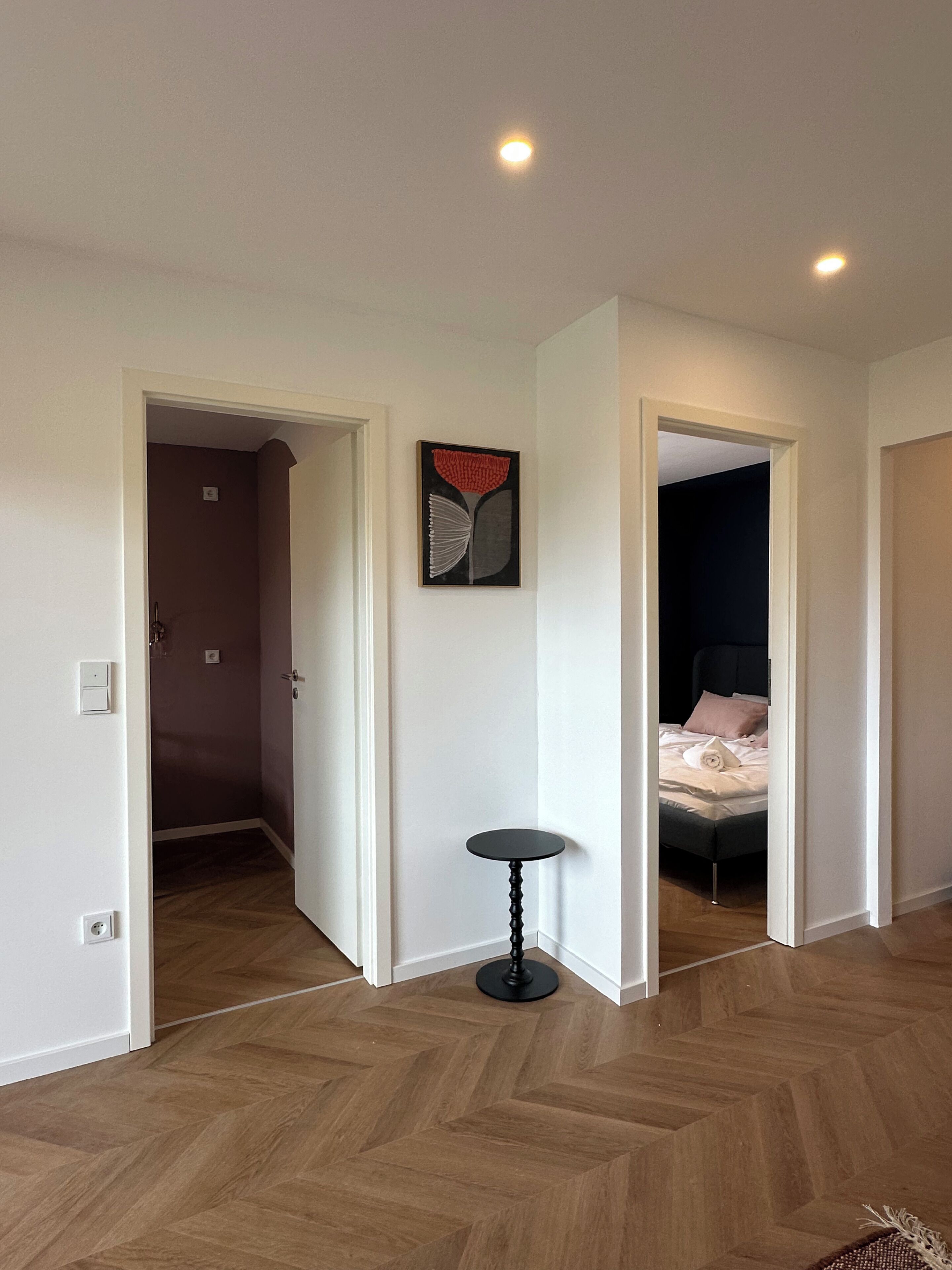A hotel room with a wooden herringbone floor, a bed with a dark headboard, and a small round table.