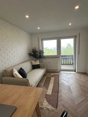 Ein modernes Wohnzimmer mit einer Couch, einem Esstisch und Blick durch ein großes Fenster.