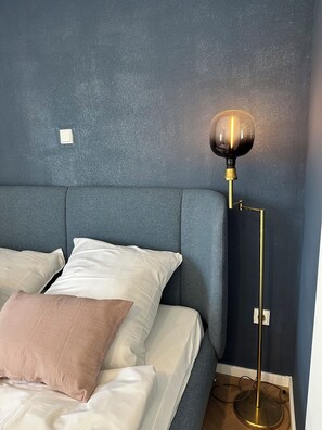 A bed with white and beige pillows, a blue headboard, and a floor lamp with a gold base.