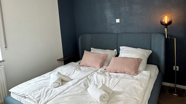 A neatly made bed with white linens and pink pillows, a bedside table with a lamp, and a dark blue accent wall. - Schönblick B7 House · Modern with a Balcony Next to the Ski Lift (Schöfweg)