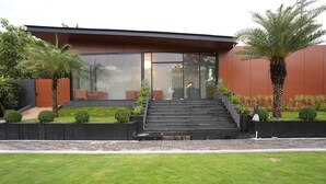 A modern building with a staircase leading to a glass entrance, surrounded by well-maintained lawns and small trees. - HF Pool Resorto (Chennai)
