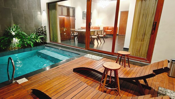 A swimming pool with a wooden deck, a bar area, and a dining area visible through a glass door. - HF Pool Resorto (Chennai)