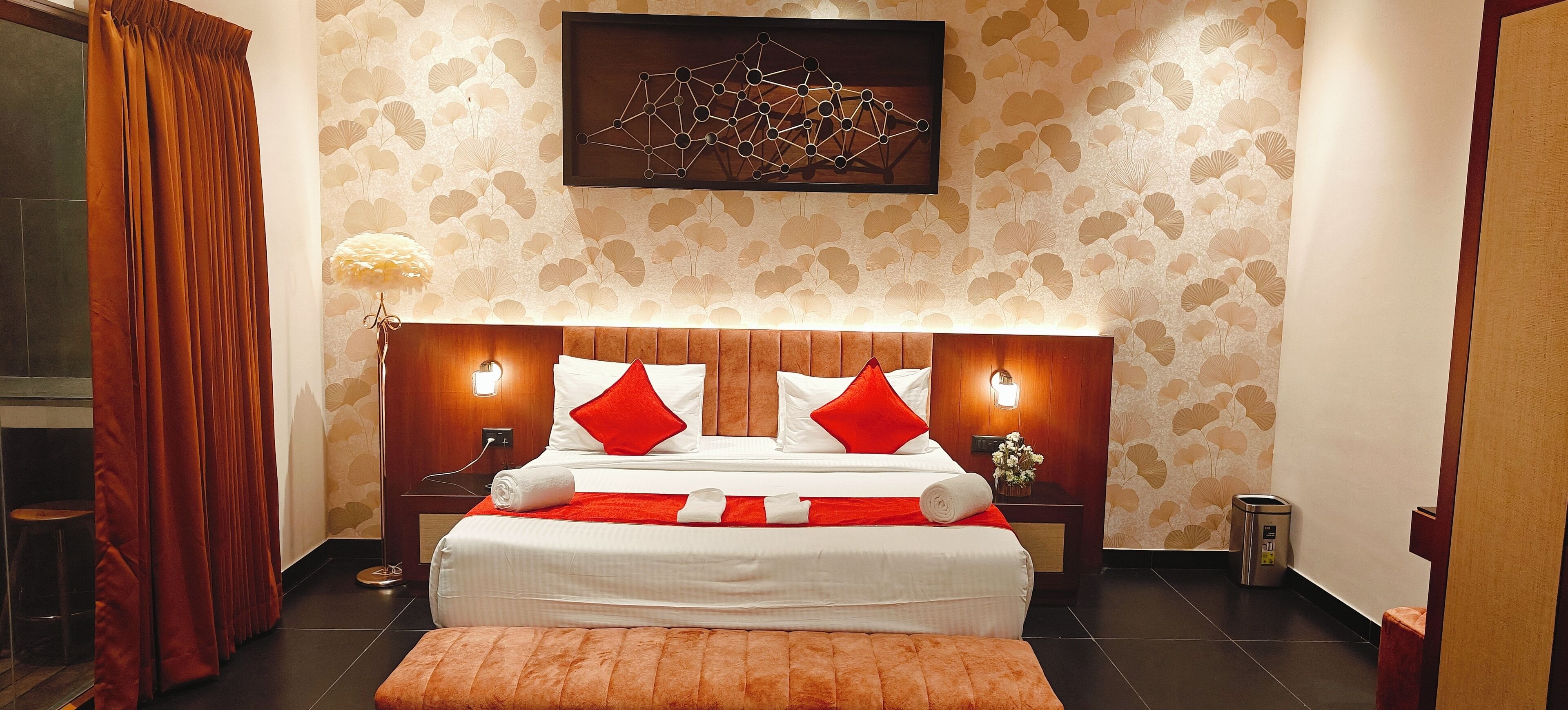 A hotel room with a large bed, a wooden headboard, two bedside lamps, and a decorative wall piece above the bed.