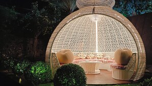 A cozy outdoor seating area with a woven dome structure, cushioned seating, and a small table. - HF Pool Resorto (Chennai)