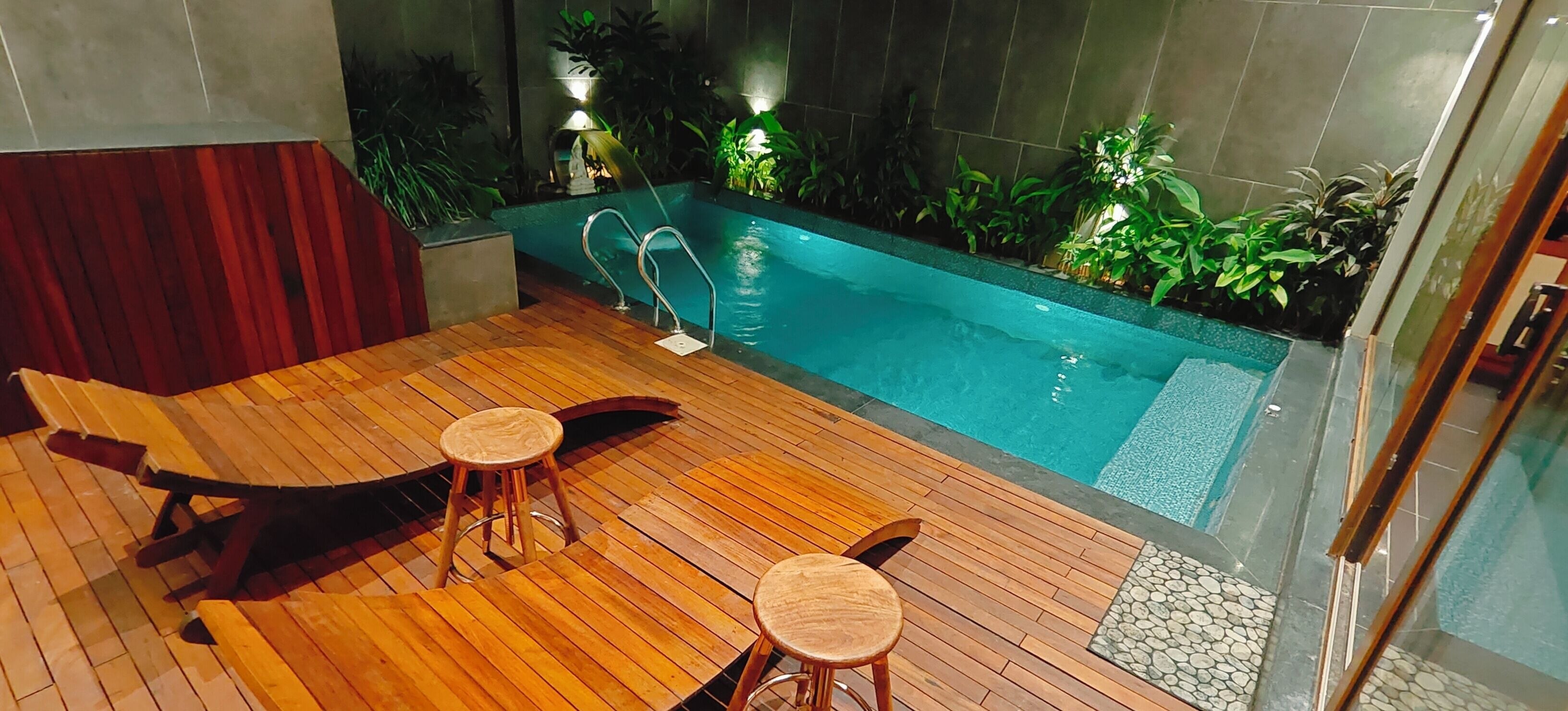 A wooden deck with two stools and a lounge chair, a small pool with a metal ladder, and potted plants around the pool.