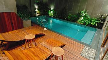 A wooden deck with two stools and a lounge chair, a small pool with a metal ladder, and potted plants around the pool.