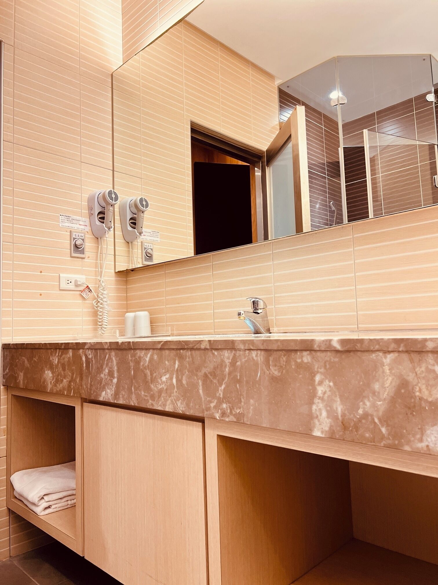 A modern bathroom with a marble countertop, wooden cabinets, and a large mirror.