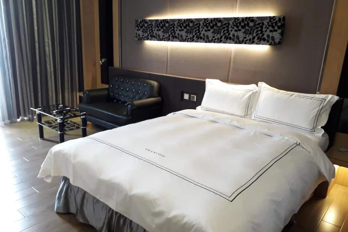 Ein ordentlich gemachtes Bett mit weißer Bettdecke und Kissen, ein schwarzes Ledersofa und ein kleiner Beistelltisch mit Tablett.