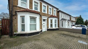 A row of terraced houses with a paved driveway and a parked car. - Drayton Green Road (London)
