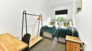 A bedroom with a bed, bedside tables, a chair, a hanging rack, and a window. - Drayton Green Road (London)