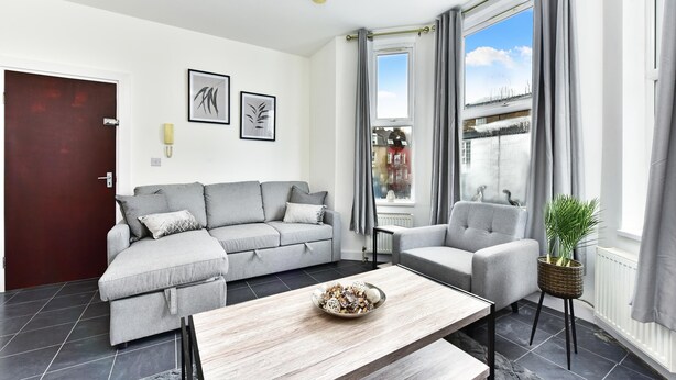 A modern living room with a grey sofa, a coffee table with decorative items, and a view of a cityscape through large windows. - Drayton Green Road (London)