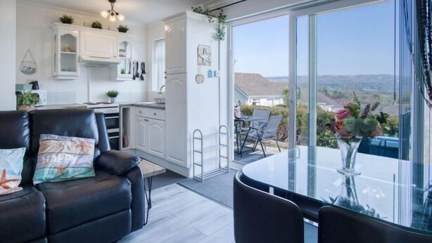 Een moderne woonkamer met een zwarte leren bank, een glazen eettafel en uitzicht op een balkon met zitplaatsen.