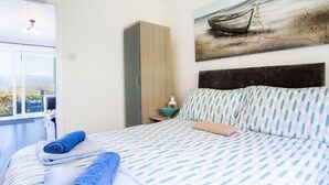 Een slaapkamer met een bed, een kledingkast, een schilderij en uitzicht door een raam.