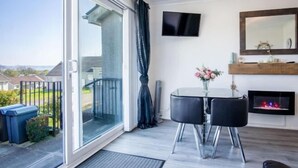 Een moderne woonkamer met een glazen deur naar een balkon, een open haard en een flatscreen televisie die aan de muur is bevestigd.
