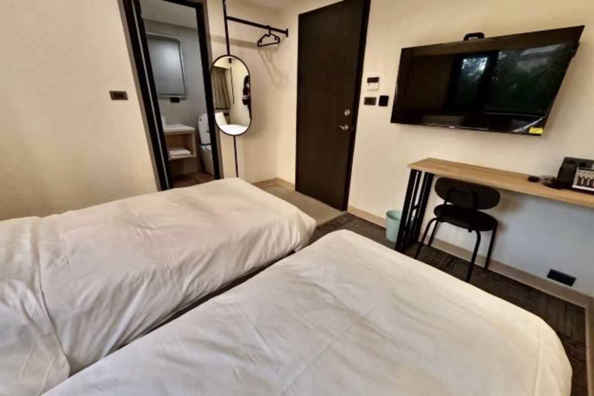 A hotel room with two beds, a desk with a chair, a TV, and a mirror.