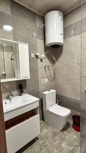 A bathroom with a white sink, mirror, toilet, and a water heater mounted on the wall.
