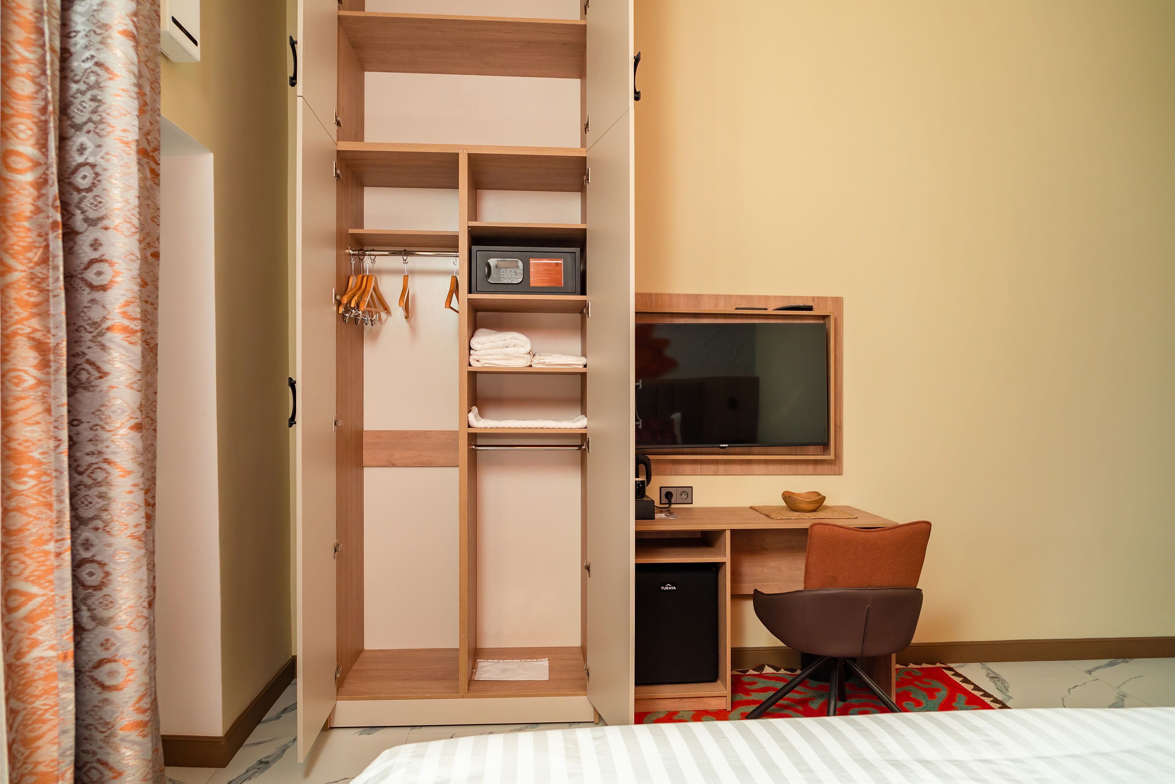A hotel room with a wardrobe, a desk with a computer, a television, and a bed.
