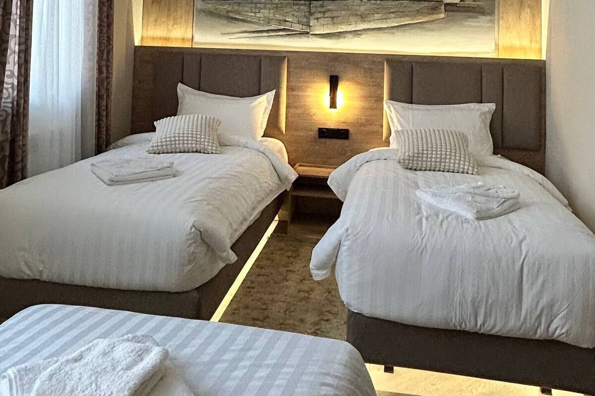 A hotel room with two beds, a large painting of a building, a chandelier, and a view of the outdoors.