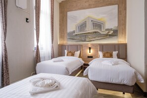 A hotel room with two beds, a painting of a building on the wall, and a nightstand with a lamp.