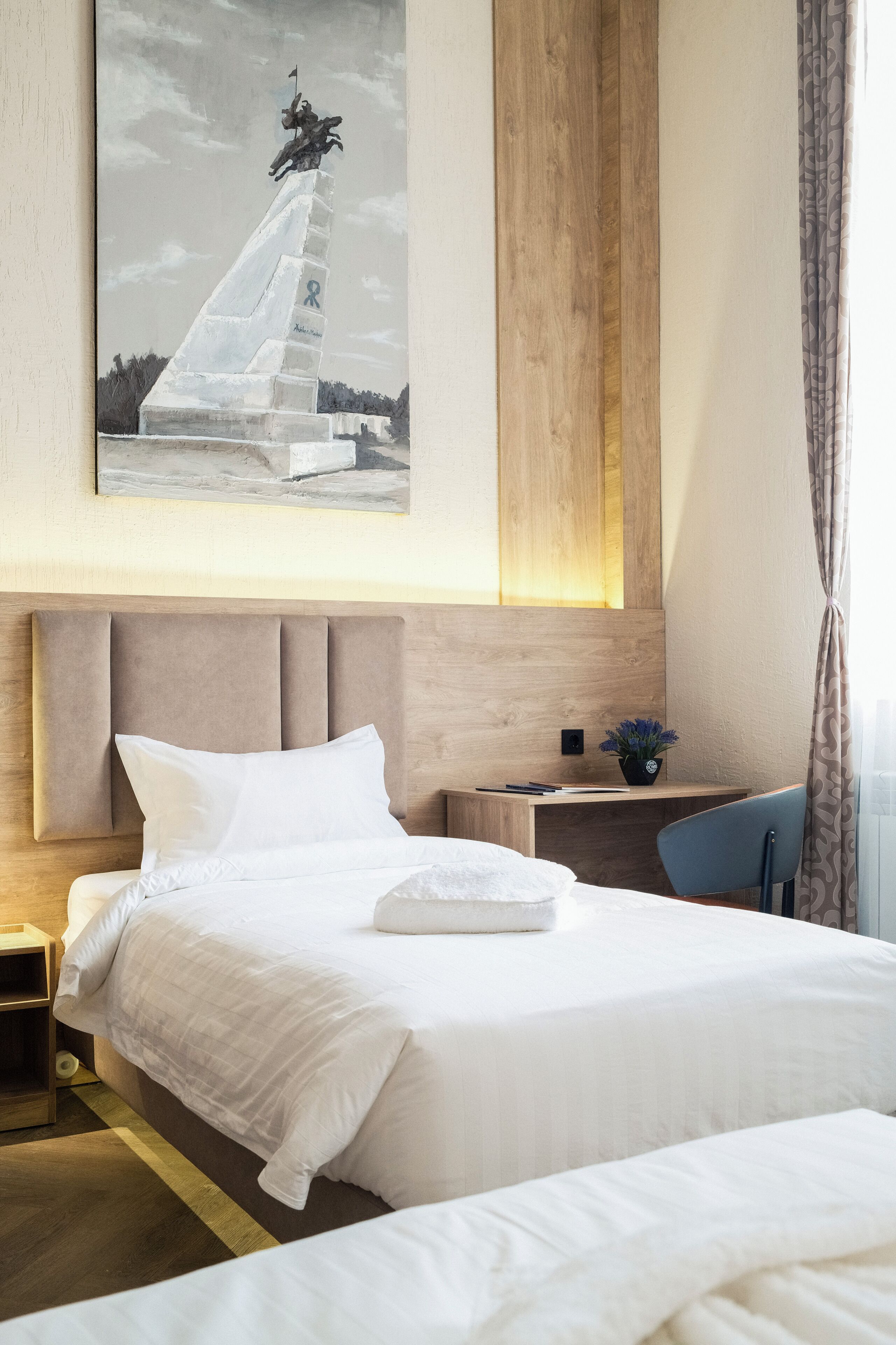 A hotel room with a bed, a desk, a chair, and a painting on the wall.
