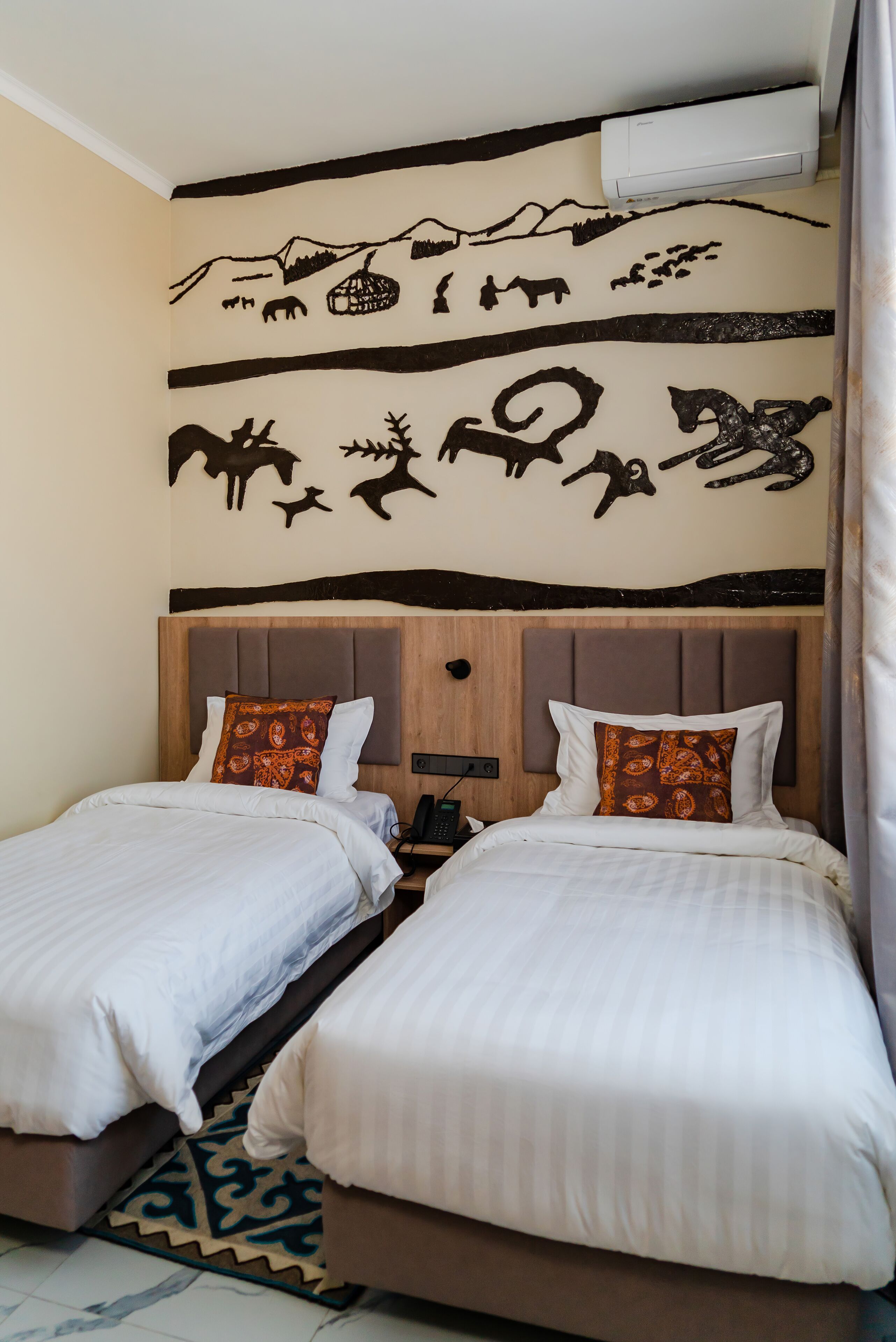 Habitació d'hotel amb dos llits, un capçal de fusta i un mural amb representació d'animals.