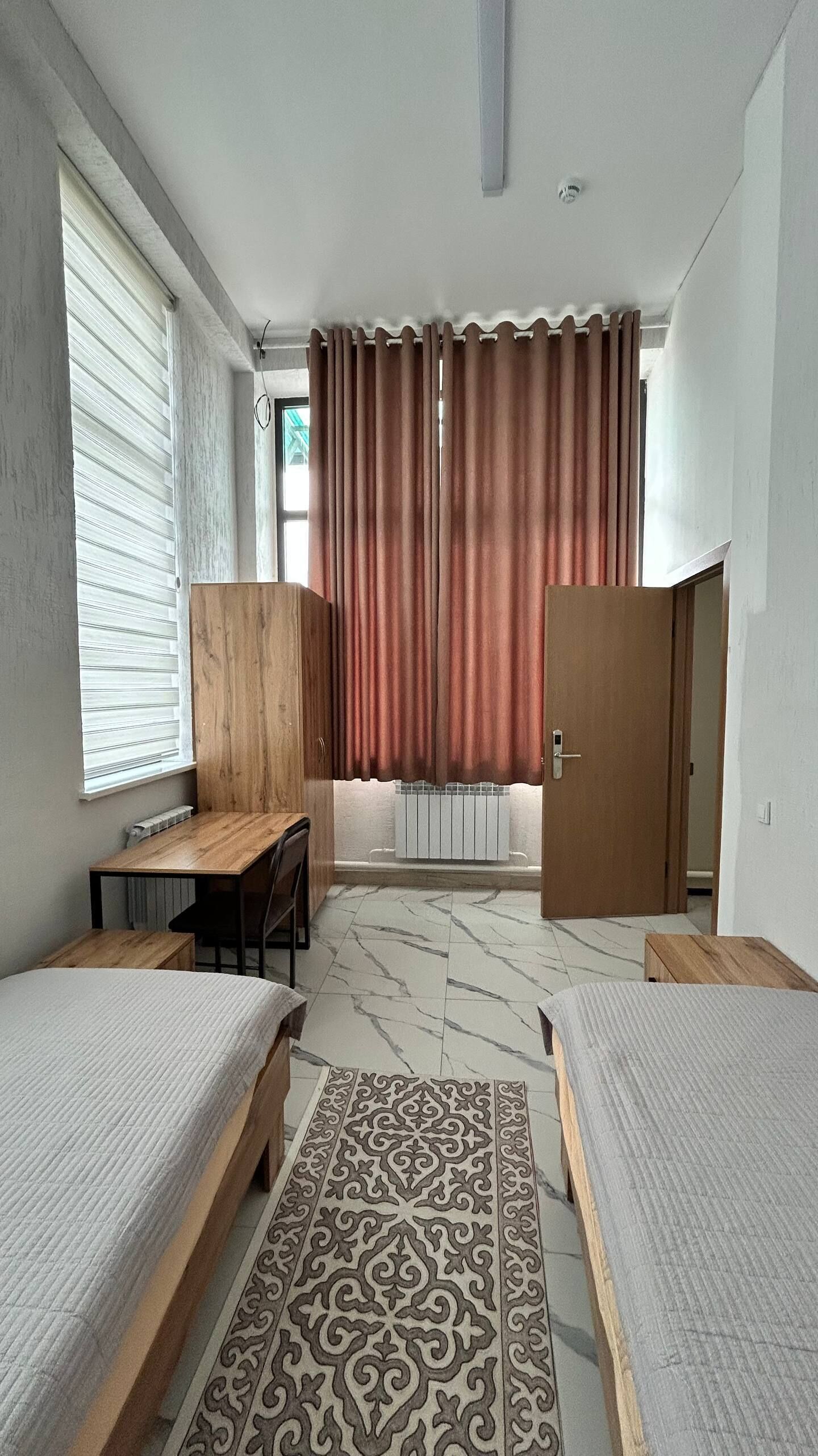 A bedroom with two beds, a wooden desk, a radiator, and a patterned rug.