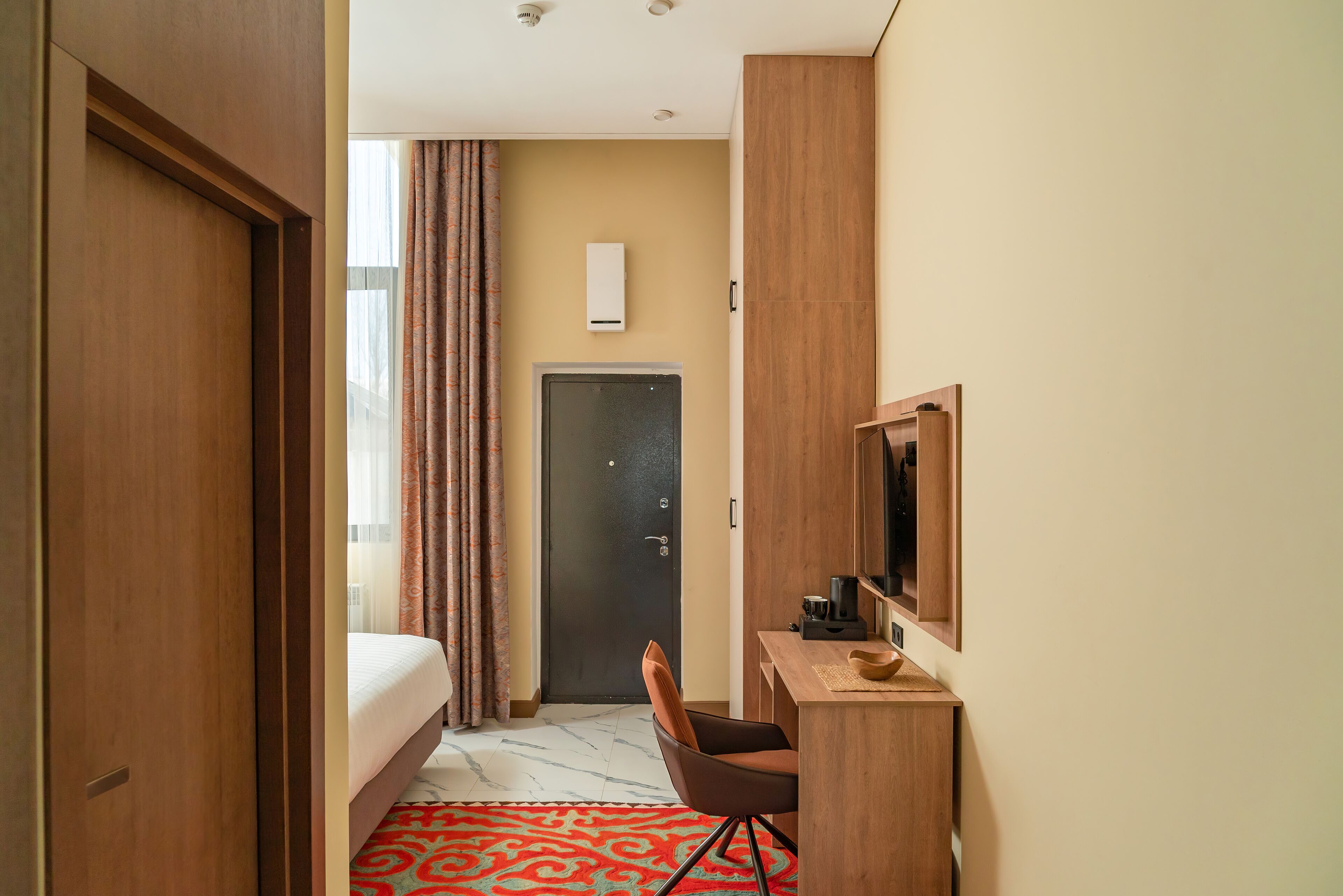 Een hotelkamer met een bed, een bureau met stoel, een televisie en een deur.